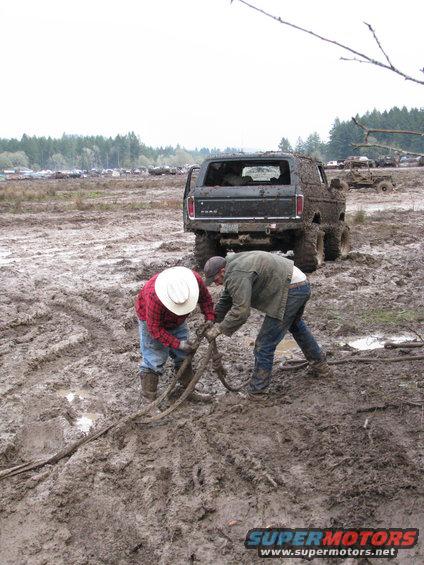 1978 Ford Bronco stuck in mud, two men pulling tow rope