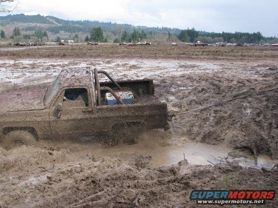 Mud-covered pickup truck stuck in a mud pit, with a tow rope attached