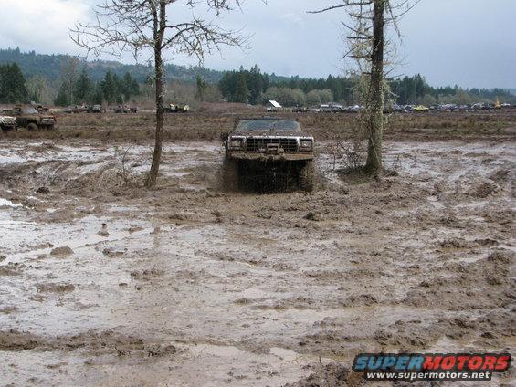 Mud-splattered off-road vehicle with winch, driving through a muddy field