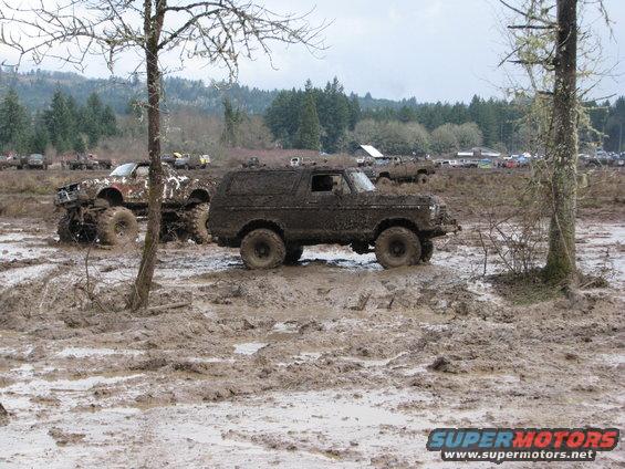 Mud-covered 1978 Ford Bronco navigating a muddy off-road course with other vehicles visible in the background