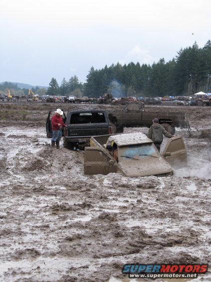 trucks stuck in mud pit, people standing around