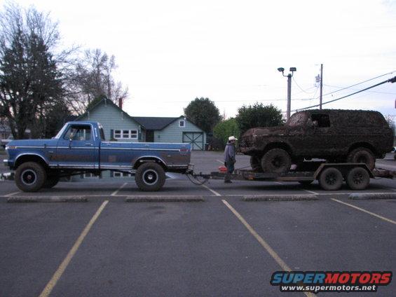 Mud-covered 1978 Ford Bronco on trailer towed by blue pickup truck