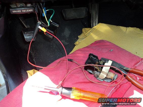 Interior view of car floor with brake release lever, wiring, and electrical testing tools