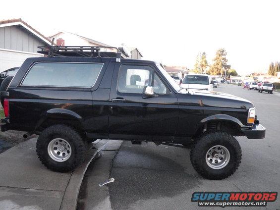 Black SUV parked on street, side view. Has a roof rack and large tires