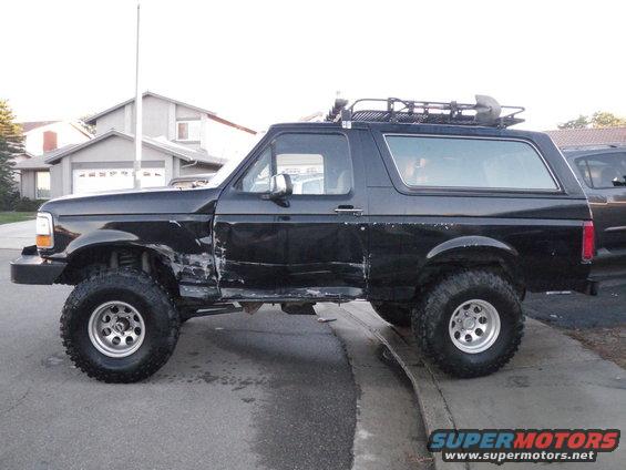 Black Ford Bronco with significant damage to the driver's side front fender and door, lifted suspension, and roof rack