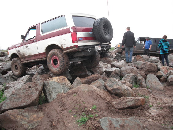 1991 Ford Bronco climbing over large rocks on an off-road trail. Another truck is visible behind it