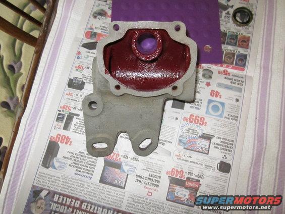 Metal part coated in red grease, resting on newspapers