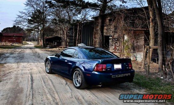 Blue Ford Mustang Cobra parked on a dirt road in front of old buildings