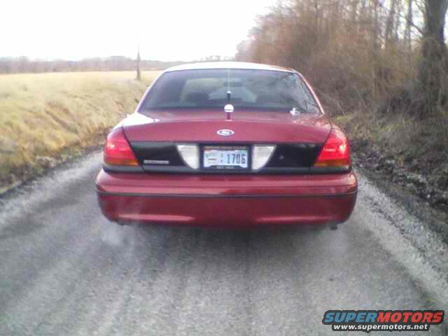 Red Ford Crown Victoria, rear view, on a dirt road. License plate 1706