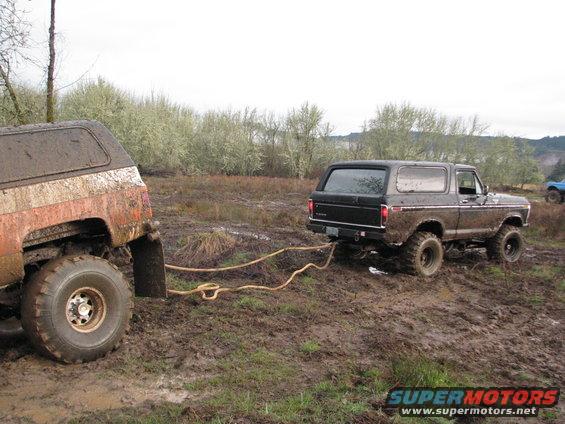 Black Ford Bronco being pulled out of mud by another off-road vehicle