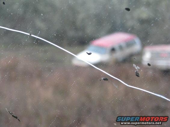 Red and white SUV seen through a cracked windshield with mud splatters