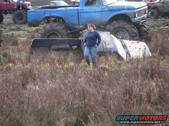 Mud bogging scene with a blue lifted truck and a white truck partially submerged in mud