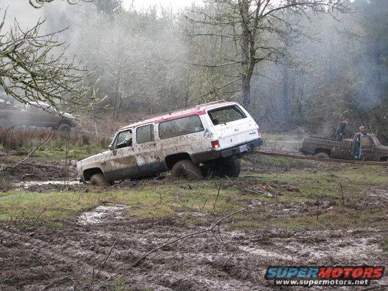 White SUV stuck in mud, being pulled by a brown pickup truck