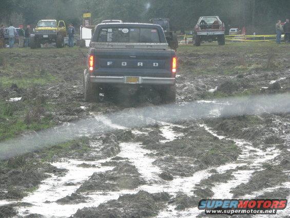 Rear view of a dark blue Ford pickup truck in mud. Muddy track ahead