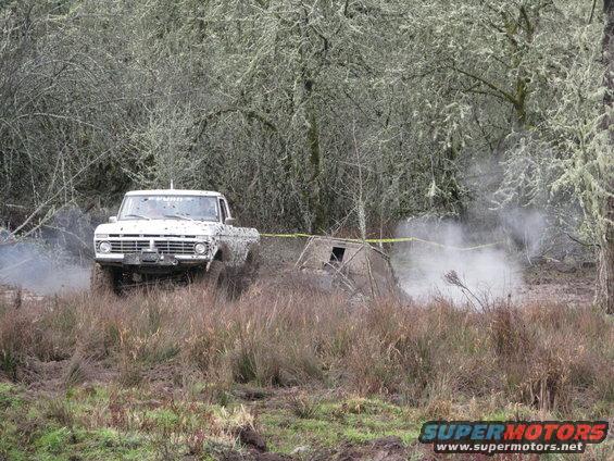 White Ford pickup truck driving through mud and brush, kicking up dust