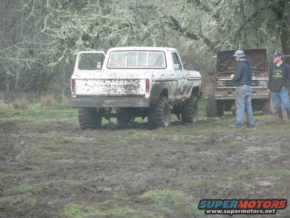 White 1978 Ford Bronco covered in mud, rear view, with driver's door open