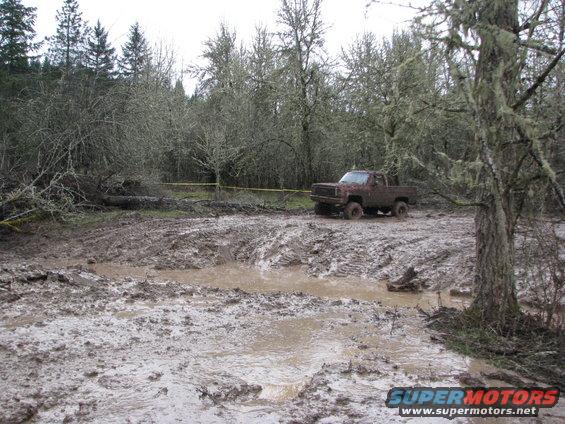 Muddy pickup truck stuck in a muddy field with trees in the background