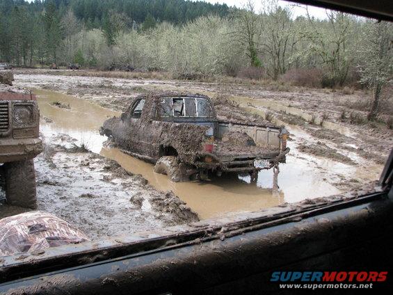 Mud-covered pickup truck stuck in mud, seen from inside another vehicle