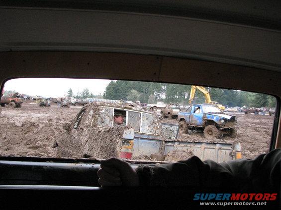 Mud bogging event with several off-road trucks stuck in mud, one blue truck in foreground