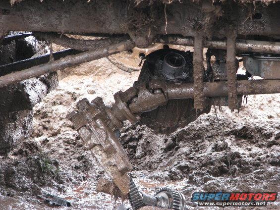 Undercarriage of a vehicle stuck in mud, showing drivetrain components
