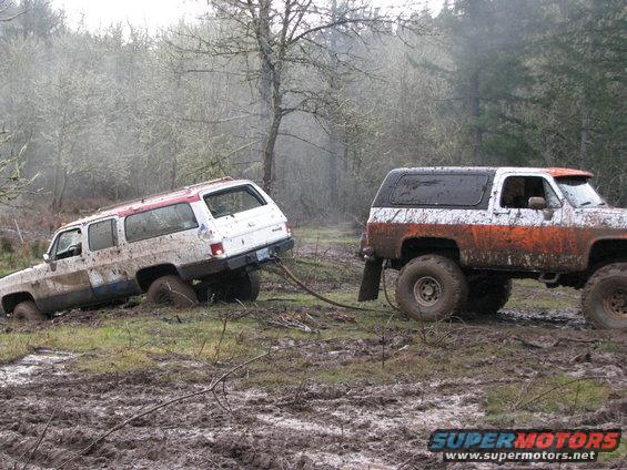 White SUV and orange/white SUV stuck in mud, being pulled by a tow strap