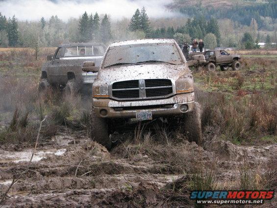 Pickup trucks driving through mud, one in foreground is a Dodge Ram