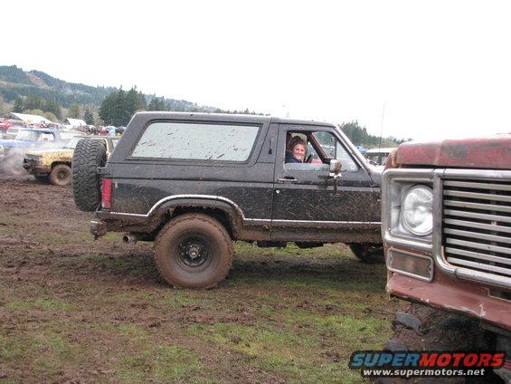 Muddy 1978 Ford Bronco with spare tire on back, driving in mud. Another vehicle is partially visible on the right