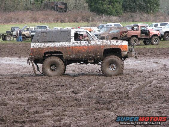 Mud-splattered white and orange SUV with large tires driving through mud