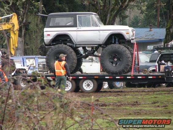 1978 Ford Bronco with massive tires on a flatbed trailer, being transported