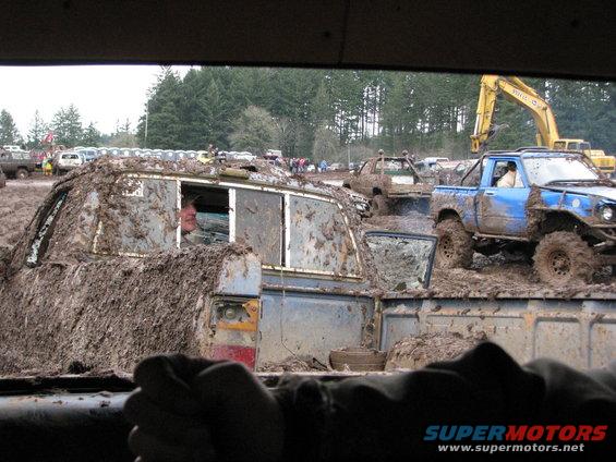 Mud-covered vehicles in off-road event, blue pickup truck prominent