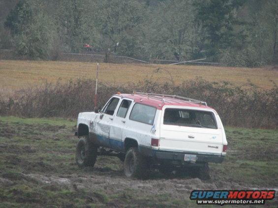 White and red SUV with lifted suspension driving through mud. License plate visible