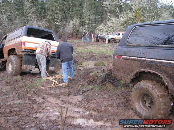 Muddy SUVs stuck in a field with people winching them