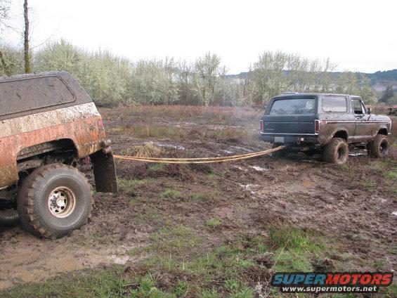 Dark 1978 Ford Bronco towing a mud-covered vehicle from a muddy field