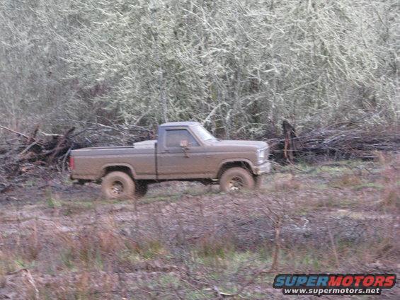 Brown Ford pickup truck driving through muddy terrain with trees in background