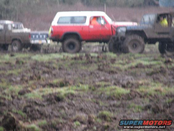 Red and white SUV with a trailer being towed by a brown pickup truck in a muddy field