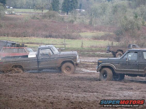 Ford Bronco and pickup truck stuck in mud, another truck in background