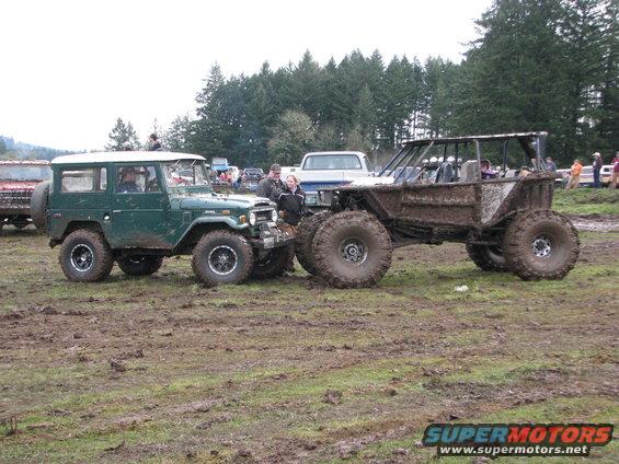 Green Toyota Land Cruiser FJ40 with a white hardtop and a custom mud bogger on large tires, both covered in mud
