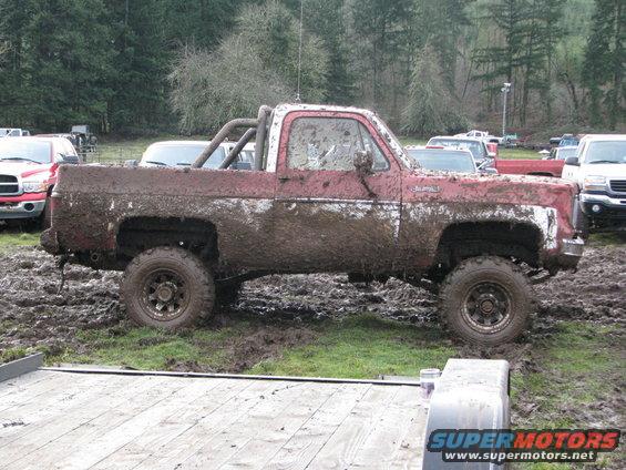 Mud-covered red and white pickup truck with roll bar, side view
