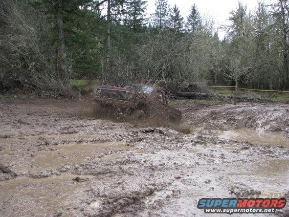 Red SUV stuck in mud, front grille visible, trees and mud in background