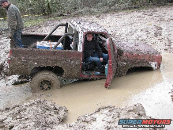 Red pickup truck stuck in mud, driver in cab, door open