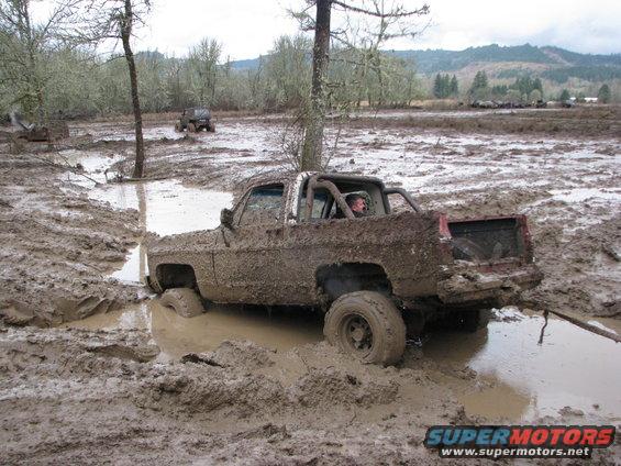 Mud-covered pickup truck stuck in a muddy field with another vehicle in the background