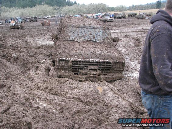 Mud-covered 1978 Ford Bronco stuck in a muddy field with other vehicles in the background