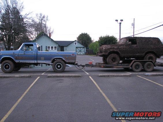 Blue pickup truck towing a trailer with a mud-covered SUV on it
