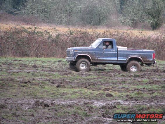 Blue pickup truck driving through mud, driver visible