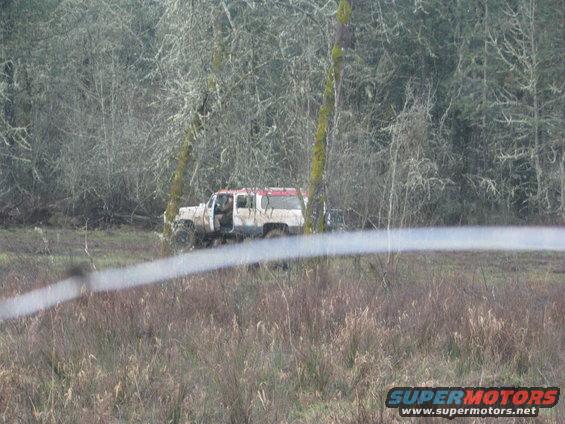 Muddy white and red SUV with doors open, parked in a field near trees