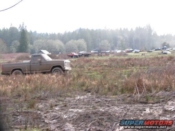 Muddy pickup truck parked in a field with other vehicles in the background