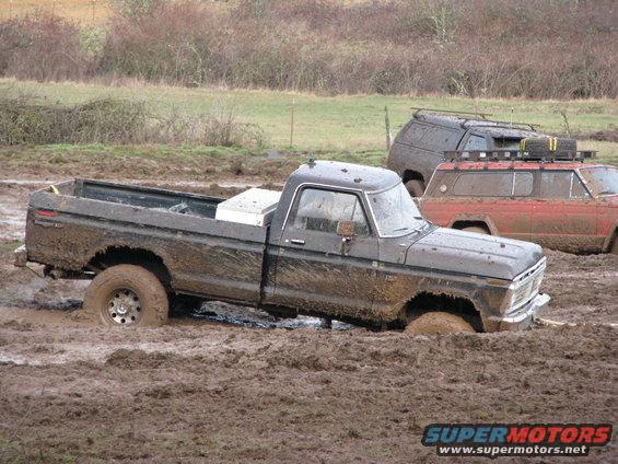 Muddy black pickup truck stuck in mud, with other vehicles behind