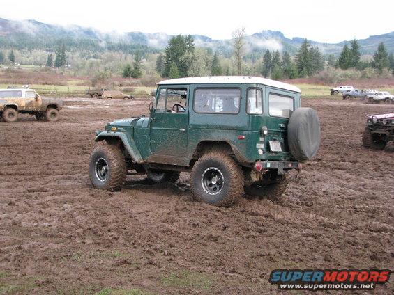 Green Toyota Land Cruiser FJ40 with white hardtop stuck in mud, rear spare tire visible