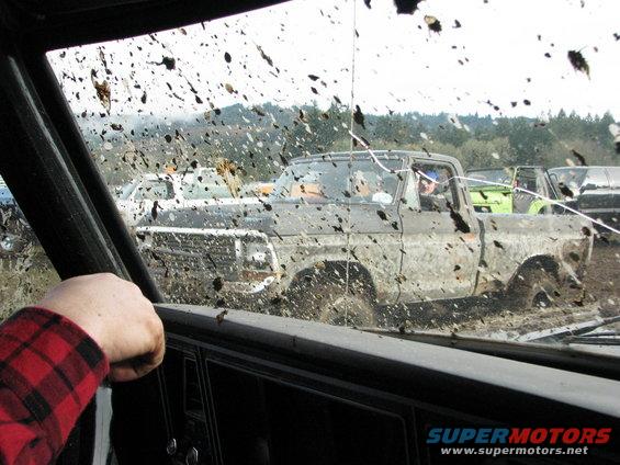 Muddy 1978 Ford Bronco driving through a mud pit with other vehicles behind it