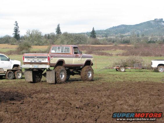 Brown and tan Ford pickup truck with large tires, towing a trailer in mud